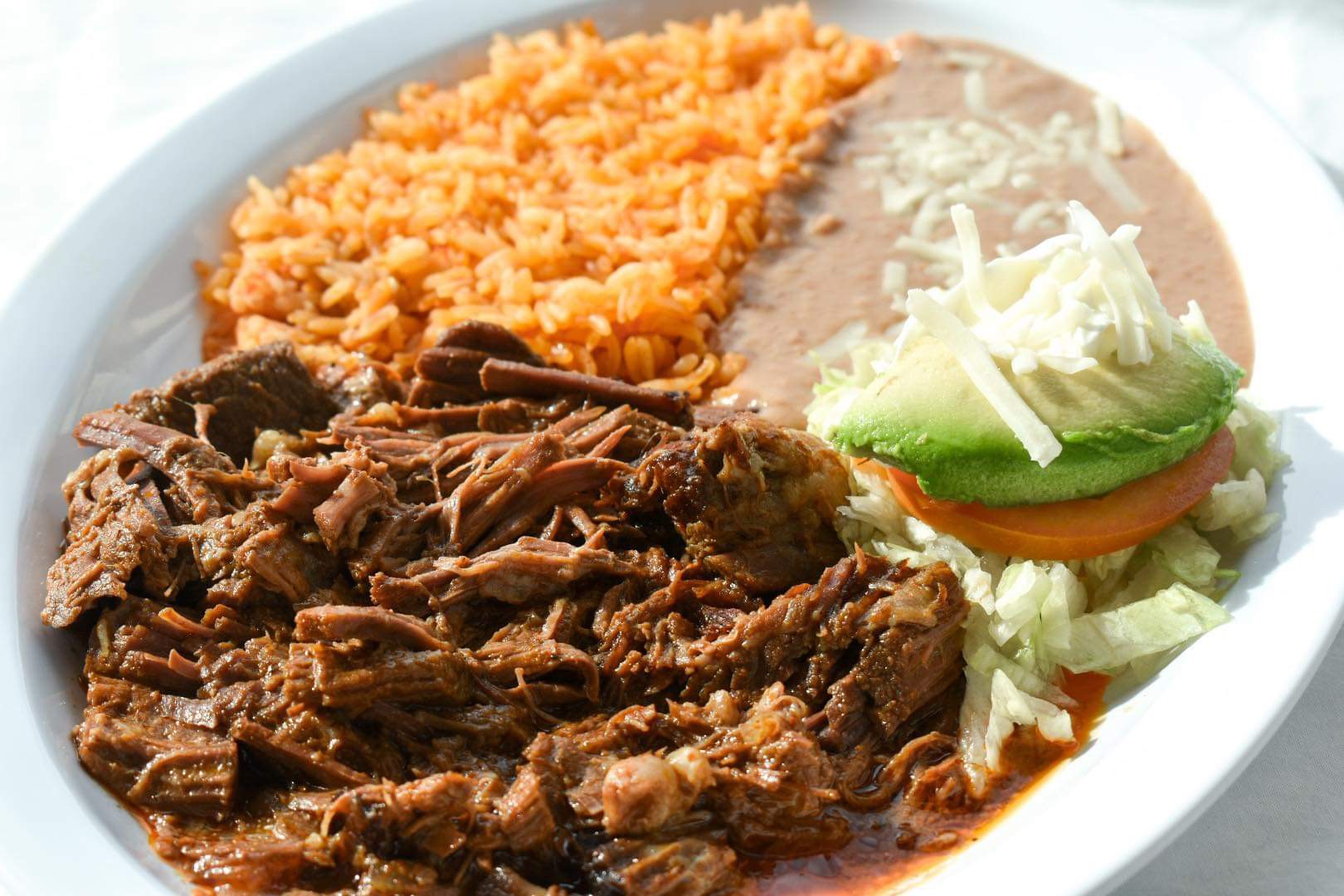 Bowl with shredded beef, rice, beans, lettuce, tomato, avocado, and cheese